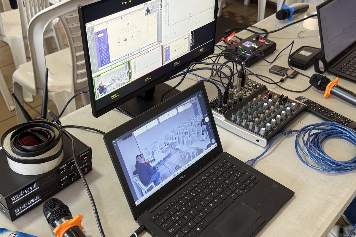 Mesa del operador técnico en una asamblea de copropietarios operada por CLICK: monitor con la vista previa de las cámaras y la gráfica de quórum, portátil con la imagen del salón, consola de sonido, micrófonos inalámbricos y receptor de los controles de votación, con las sillas del salón detrás